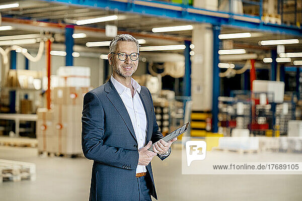 Smiling businessman with tablet PC standing at warehouse