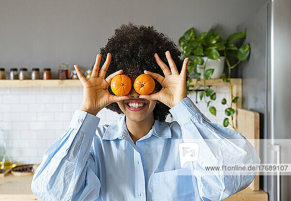 Young woman holding oranges in front of eyes at home
