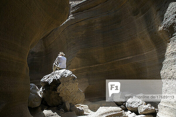 Tourist sitzt auf einem Felsen in der Wüstengegend auf Gran Canaria  Barranco De Las Vacas  Spanien