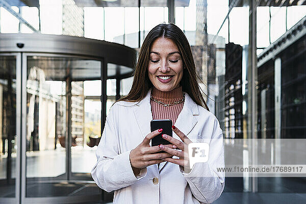 Happy businesswoman using mobile phone at office building
