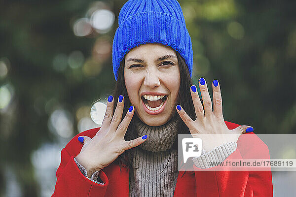 Young woman wearing blue knit hat gesturing with mouth open