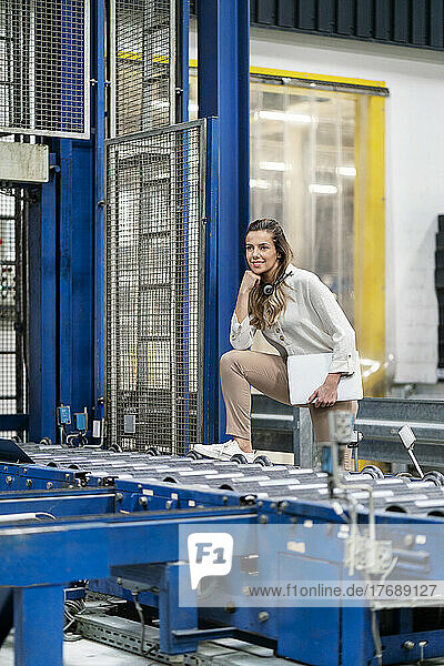 Young businesswoman with leg on conveyor belt in factory