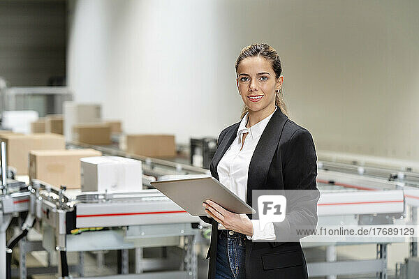 Confident businesswoman with tablet computer at factory