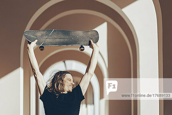 Mann mit langen Haaren hebt Skateboard über Kopf in Spielhalle