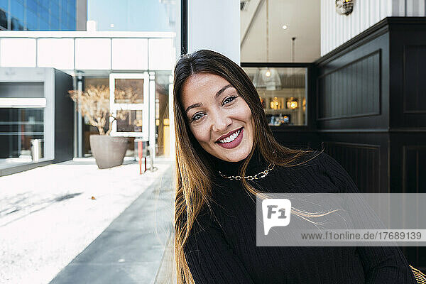 Smiling woman with long hair leaning head on glass wall at cafe