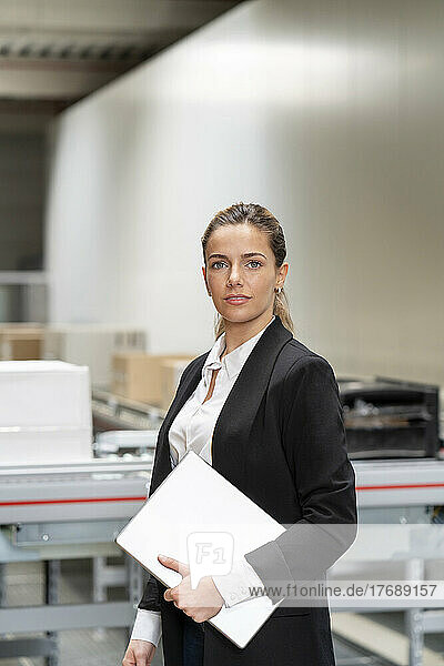 Confident businesswoman with tablet PC standing in factory