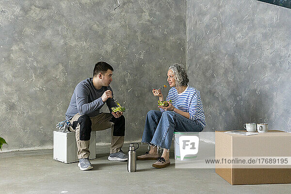 Woman with friend having lunch together sitting in front of wall at new home