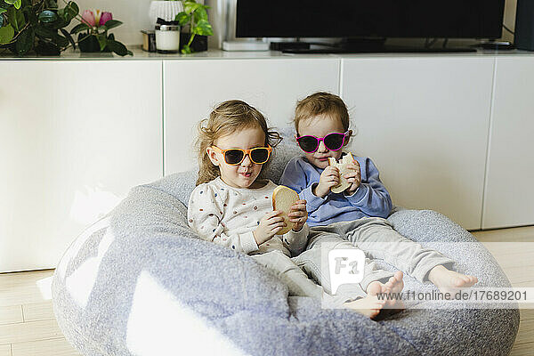 Twin sisters wearing sunglasses eating bread at home