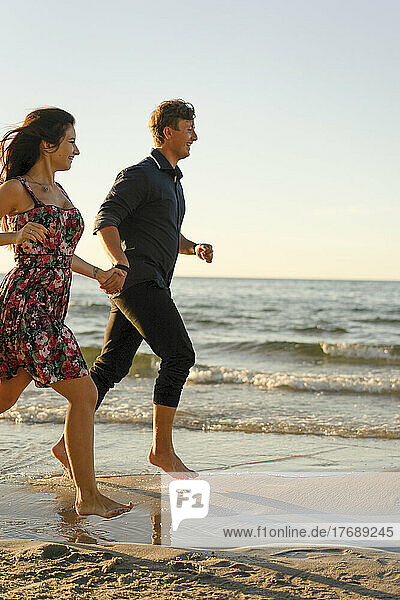 Happy couple holding hands running at beach on sunny day