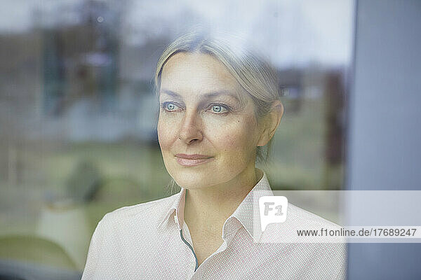 Smiling woman with blond hair looking through glass window