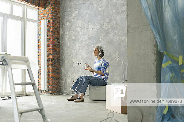 Woman taking lunch break sitting on box in front of wall