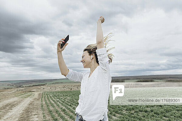 Woman dancing and listening music through smart phone in agricultural field