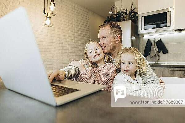 Lächelnder Geschäftsmann mit Töchtern  die zu Hause Laptop benutzen