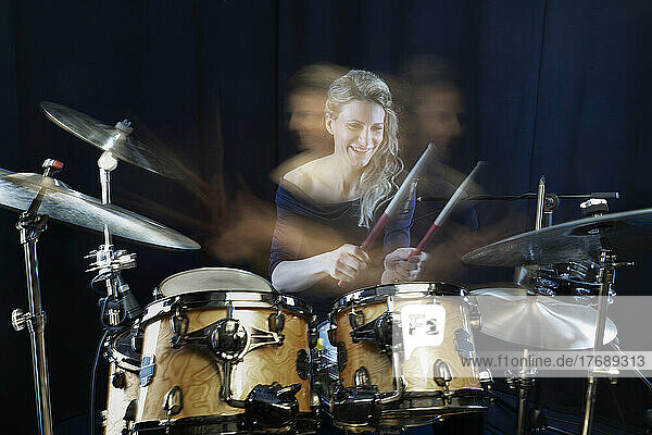 Happy drummer playing drum kit against black background