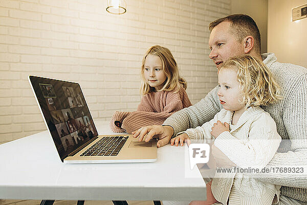 Businessman using laptop sitting with daughters at home
