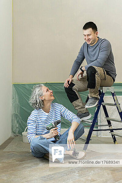 Happy woman sitting by friend on ladder at home
