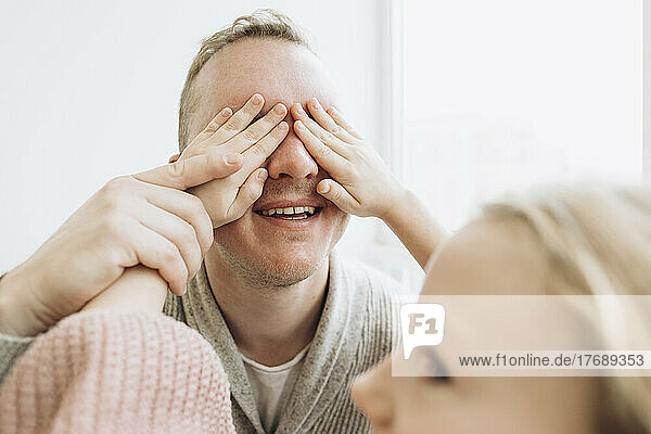 Daughter covering eyes of father with hands at home