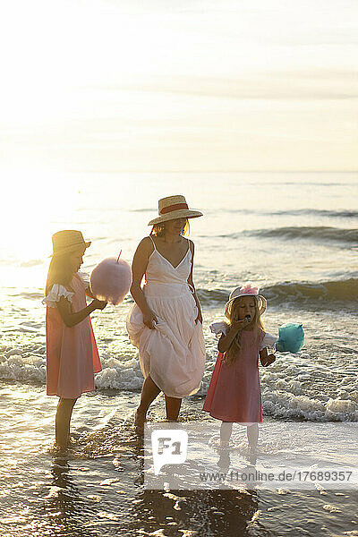 Mutter mit Töchtern isst an einem sonnigen Tag am Strand Zuckerwatte