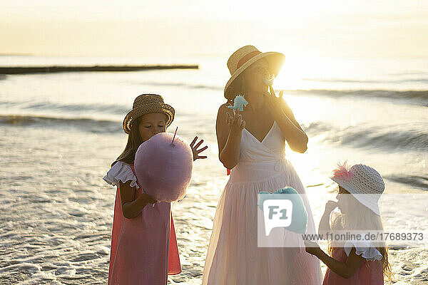 Mother and daughters eating cotton candy at beach on sunny day
