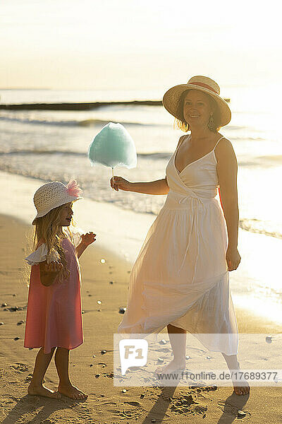 Glückliche Mutter schenkt ihrer Tochter am Strand Zuckerwatte