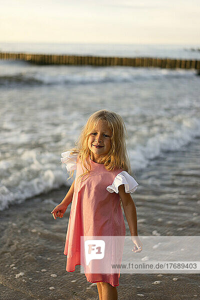 Smiling cute girl with blond hair standing at beach