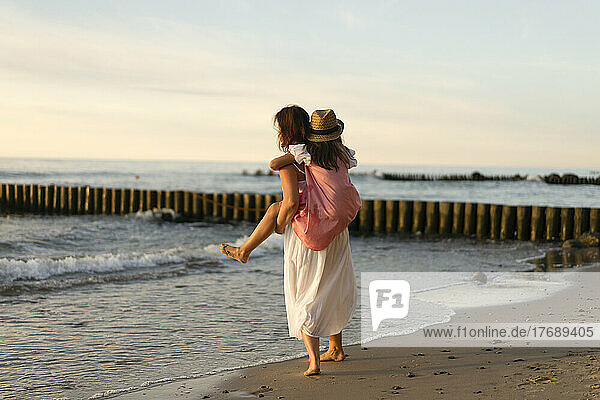 Mother giving piggyback ride to daughter at beach