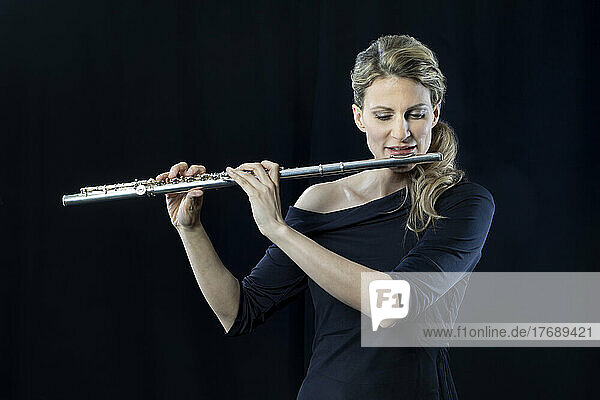 Mature woman playing flute against black background