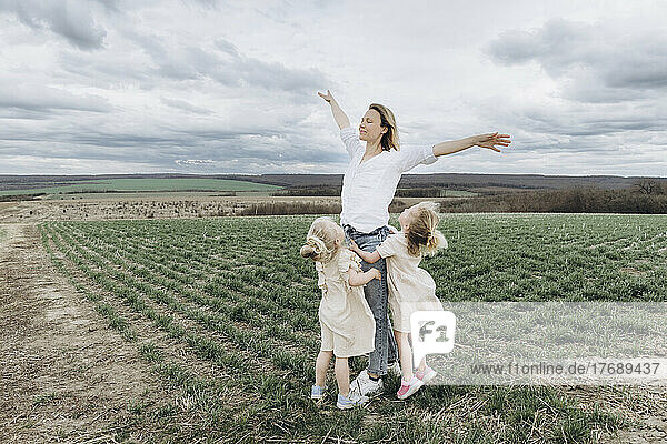 Carefree woman with arms outstretched standing with daughter in agricultural field