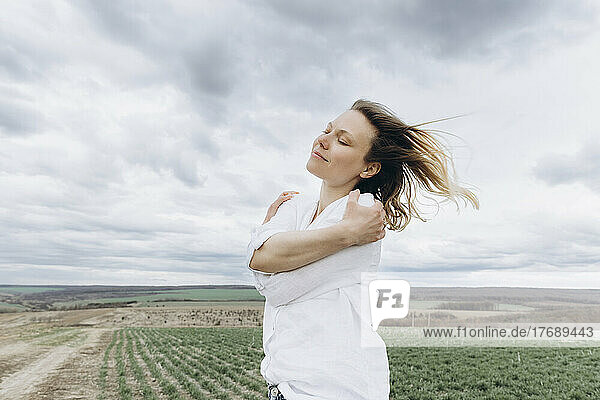 Woman with eyes closed hugging self in agricultural field