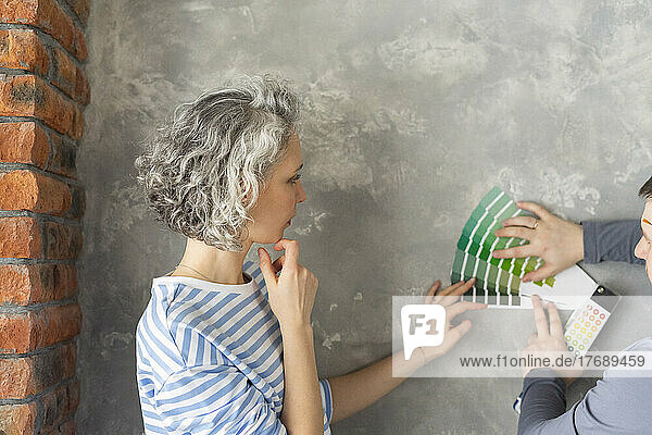 Woman with friend choosing color from swatch chart on gray wall
