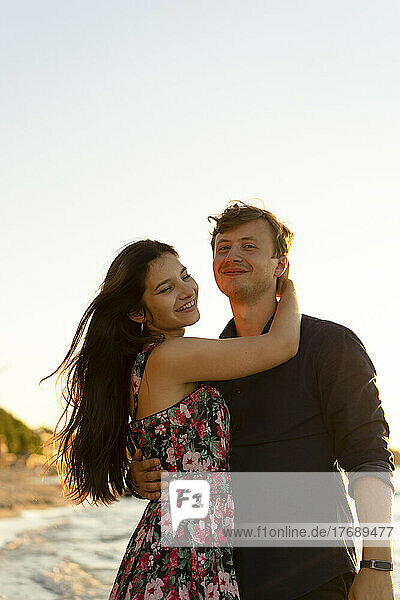 Happy young couple standing at beach on sunny day