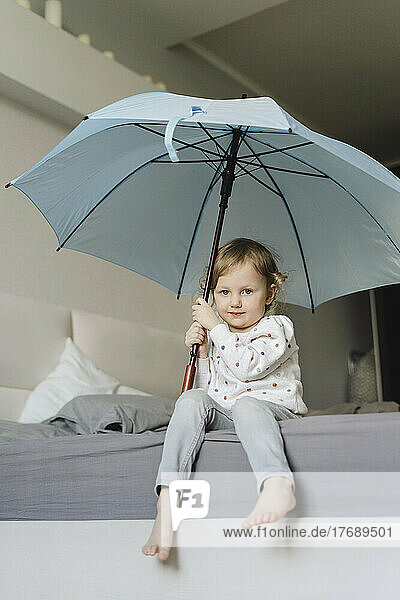 Innocent girl sitting with umbrella in bedroom