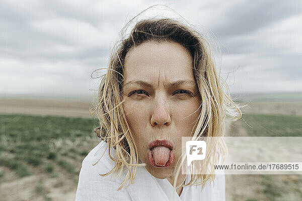 Playful woman sticking out tongue at agricultural field