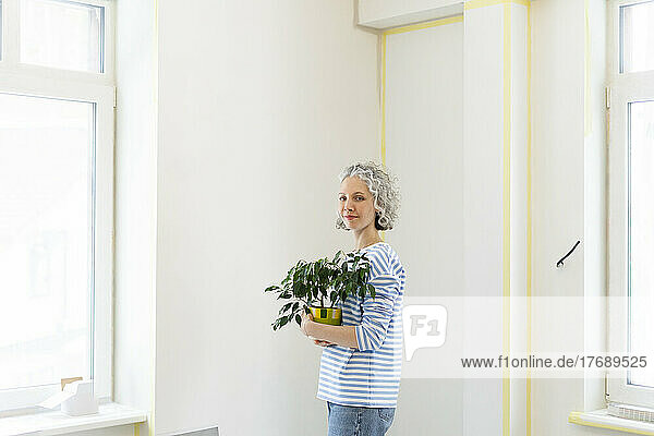 Woman with potted plant standing in front of white wall