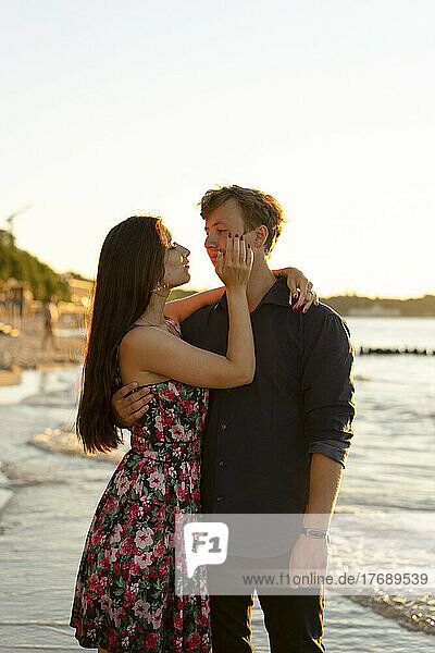 Young woman embracing boyfriend at beach of sea on sunny day