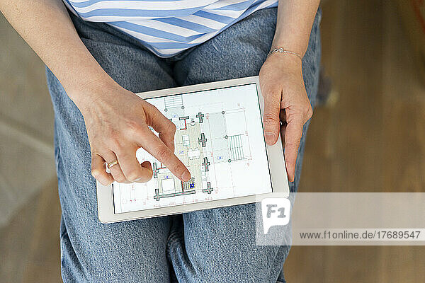 Hands of woman holding tablet PC examining blueprint of home