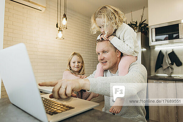 Girl sitting on father's shoulder working at home