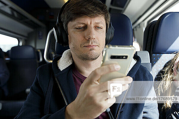 Man wearing wireless headphones using mobile phone in train
