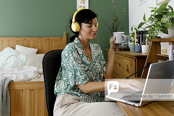 Smiling businesswoman listening music through headphones using laptop at home