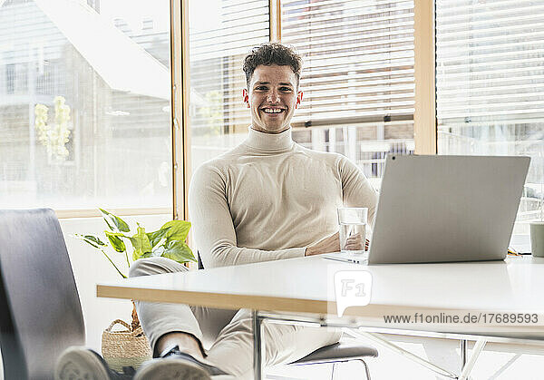 Smiling young businessman with laptop at desk in office