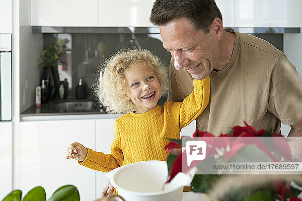 Happy blond girl baking with father in kitchen at home