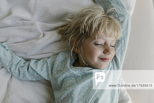Smiling girl with eyes closed lying on bed at home