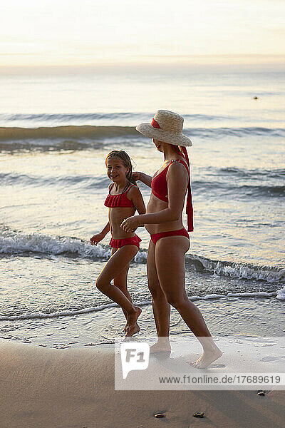 Mutter und Tochter tragen Badebekleidung und gehen am Strand spazieren