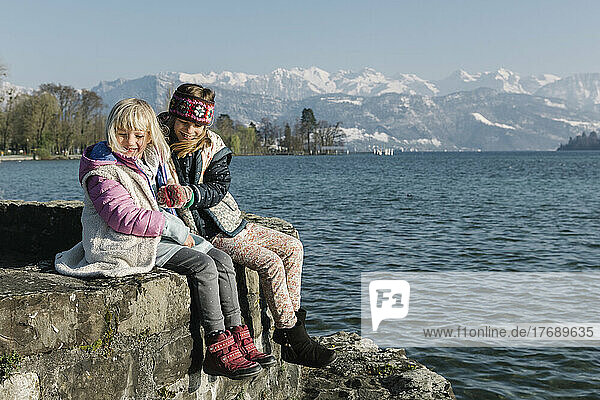 Happy sisters sitting on wall by lake