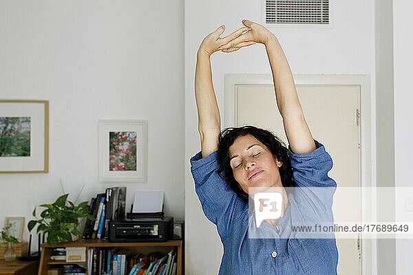 Woman with eyes closed stretching arms at home
