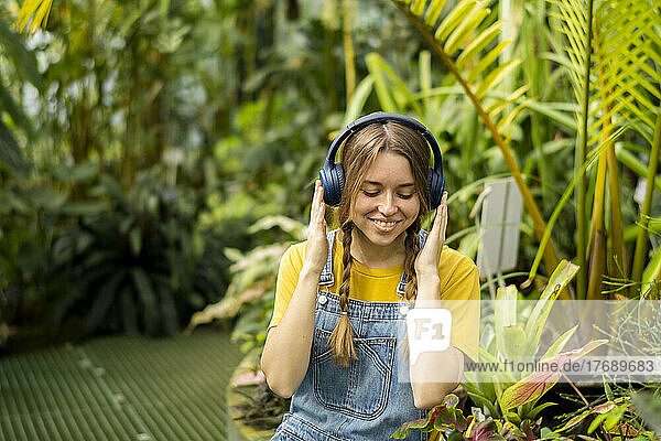 Happy woman enjoying music through wireless headphones sitting in garden