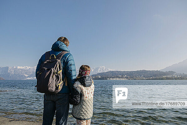 Father wearing backpack standing with daughter in front of lake