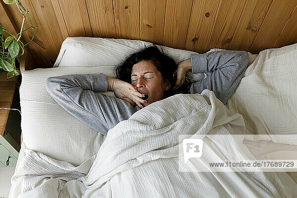 Woman with eyes closed yawning in bed at home