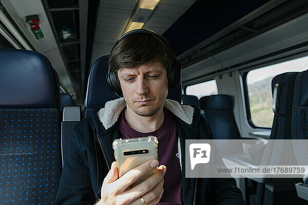 Man with headphones using smart phone sitting on seat in train