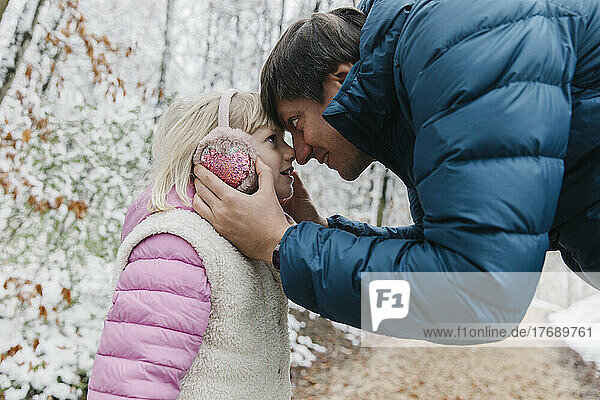 Father and daughter touching noses in winter forest